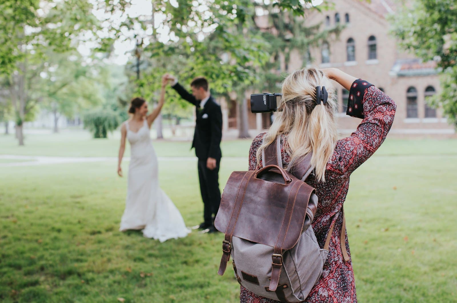 Photographer with a backpack photographing a bride and groom on a lawn
