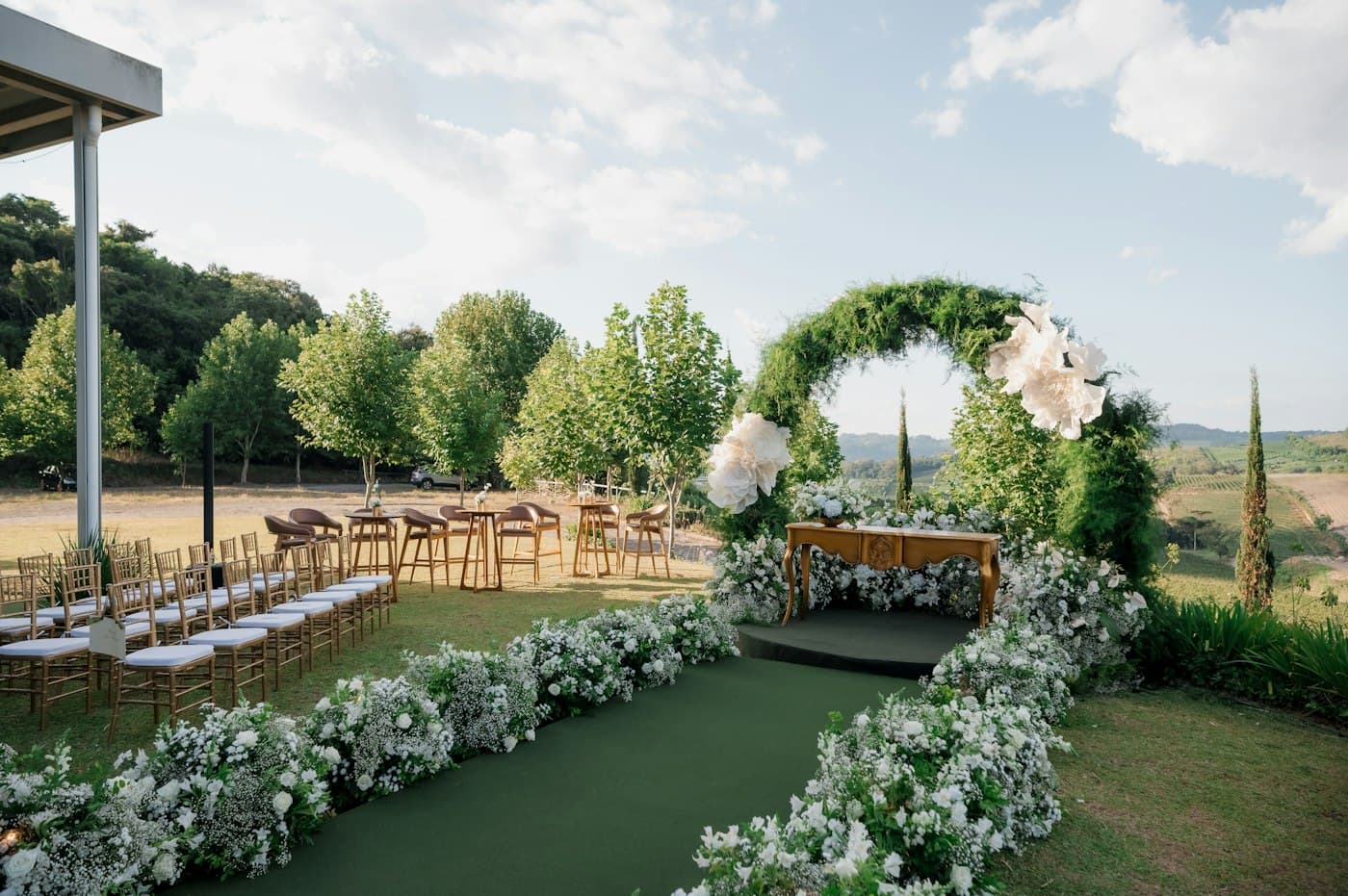 Outdoor wedding ceremony with a flower-lined aisle and a greenery arch