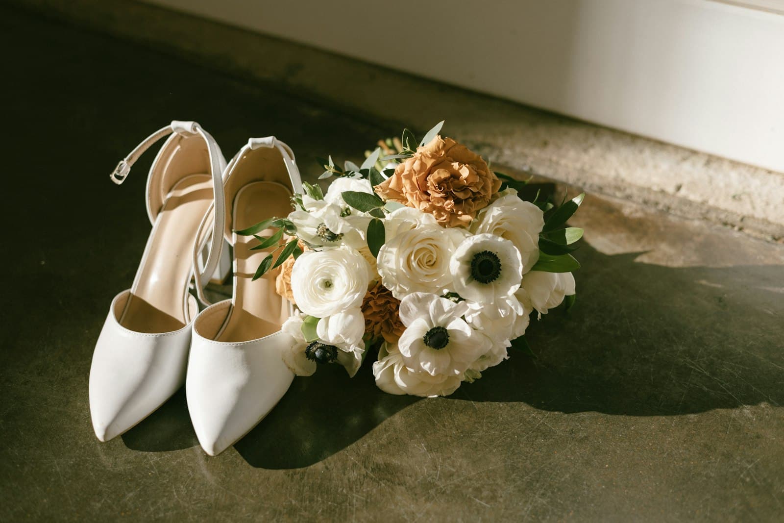 White wedding shoes beside a bouquet of white and peach flowers