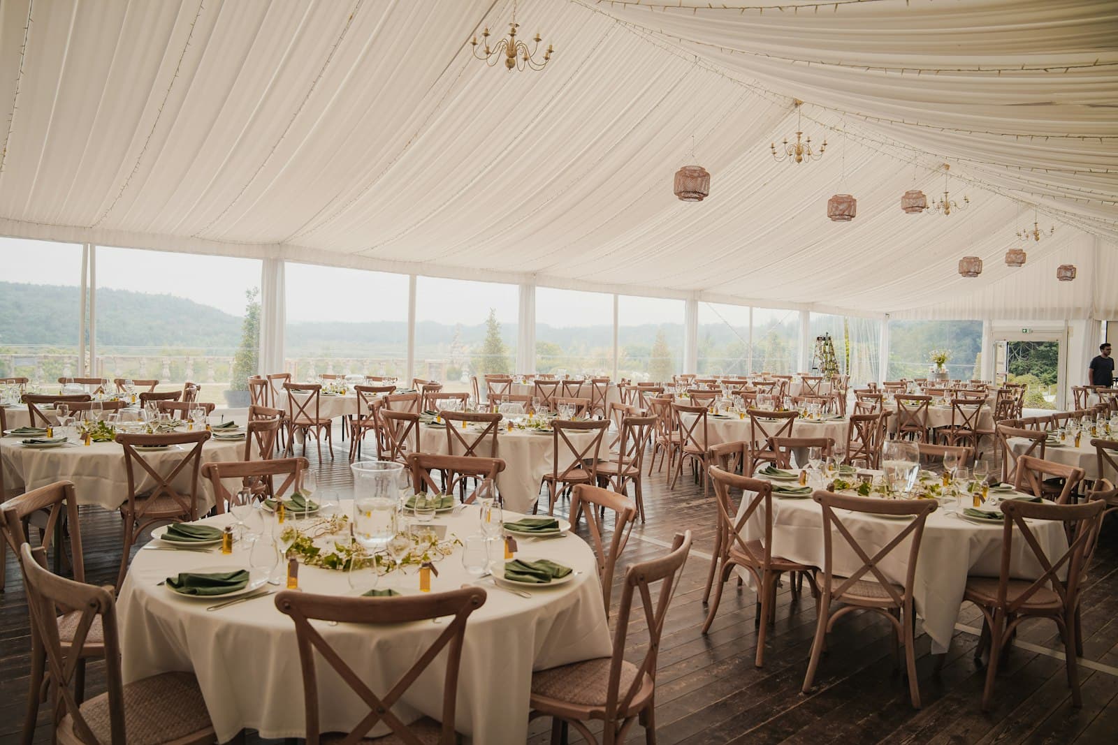 Wedding reception tent with round tables, wooden chairs and a draped ceiling
